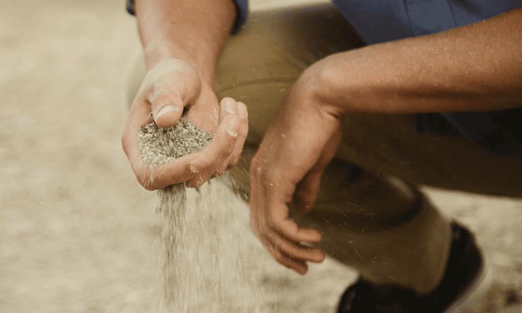 man sifting soil through hand whilst squatting down